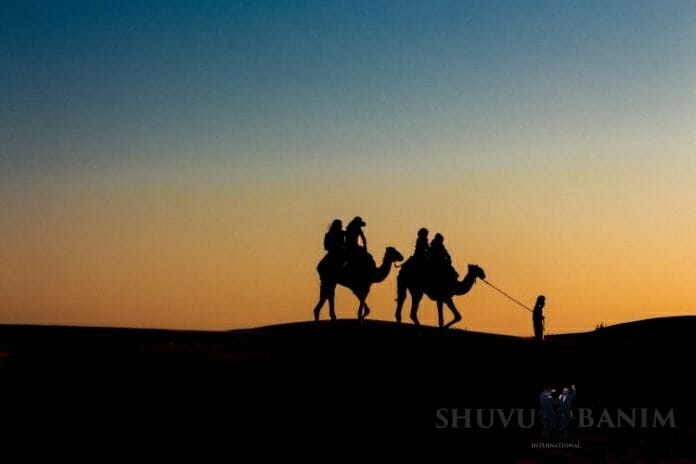 Picture of two people in silhouette riding camels in the desert